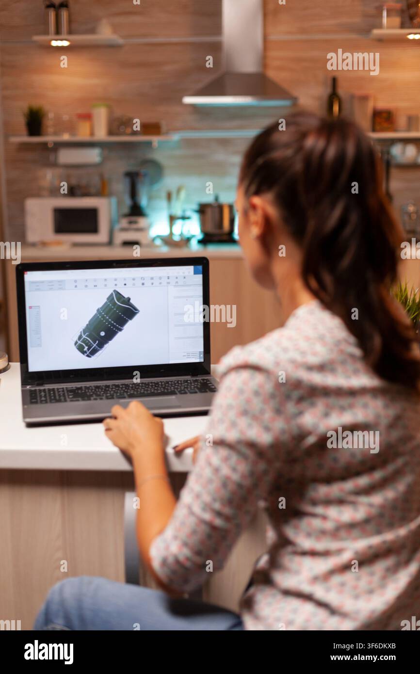 Visto da dietro, un ingegnere industriale sviluppa un progetto di turbina con software CAD su un personal computer in un ufficio domestico di notte. Foto Stock