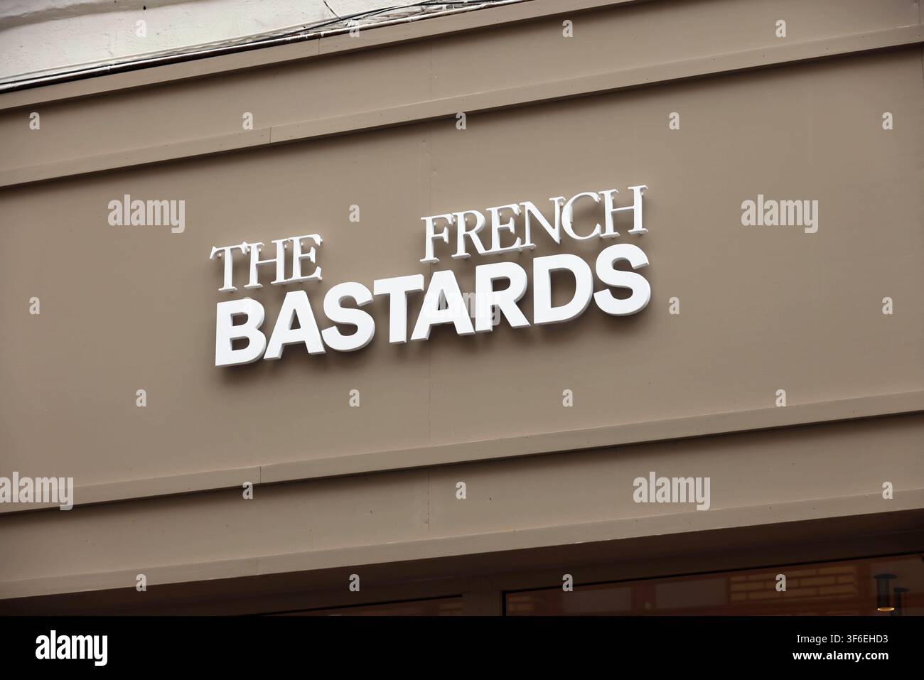 Insegna per ristorante o bar con lettere bianche in grassetto per i bastardi francesi su una facciata di edificio marrone, attività commerciale urbana e branding. Tipografia moderna Foto Stock