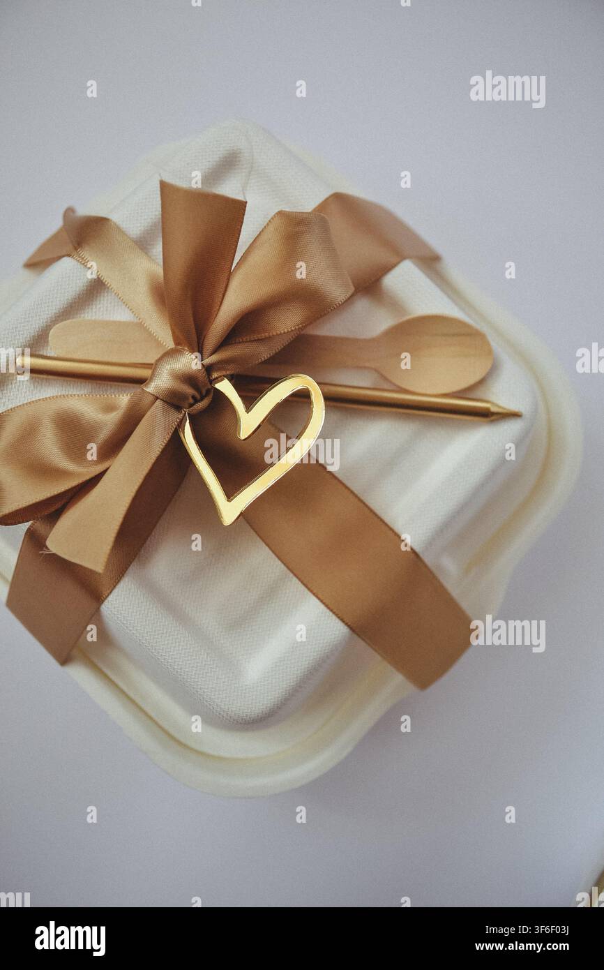 Scatola da asporto per torta bento ecologica decorata con nastro di raso, candela dorata, cucchiaio di legno e topper a forma di cuore Foto Stock