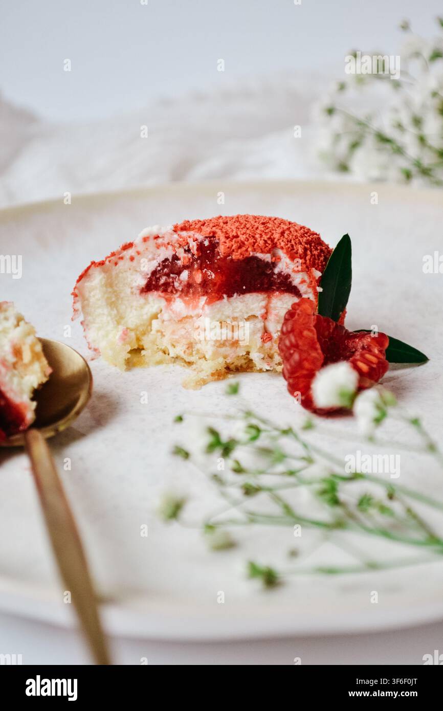 Sezione tagliata di torta mousse vellutata rossa con ripieno di gelatina di bacche, decorata con lamponi freschi e fiori Foto Stock