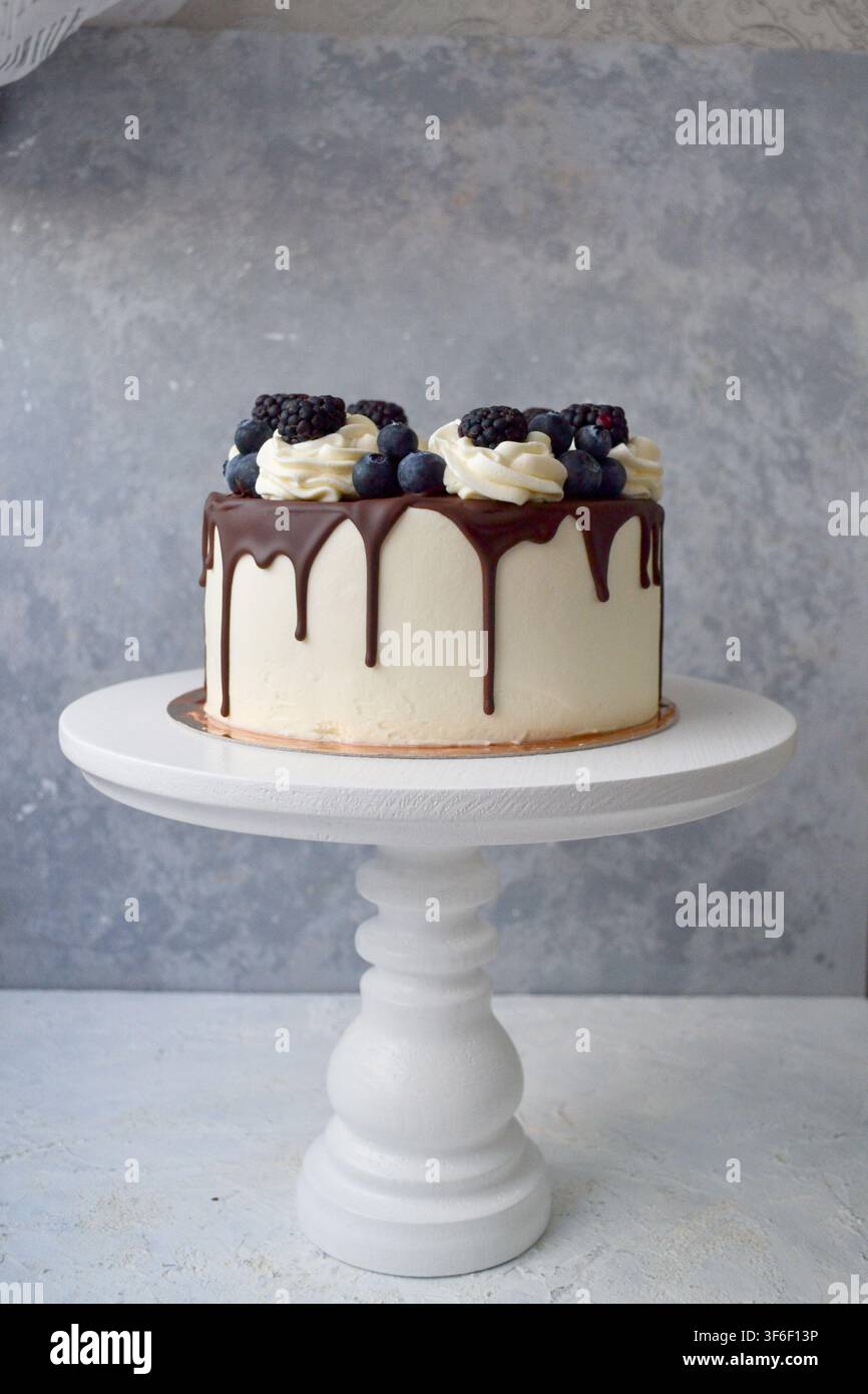 Torta a gocce bianca con ganache al cioccolato, spirali di panna montata, mirtilli e more su supporto Foto Stock