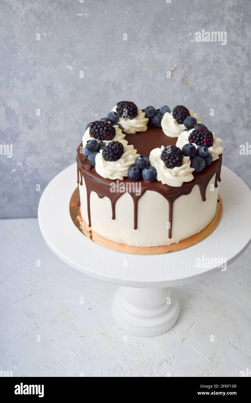 Torta a gocce bianca con ganache al cioccolato, spirali di panna montata, mirtilli e more su supporto Foto Stock