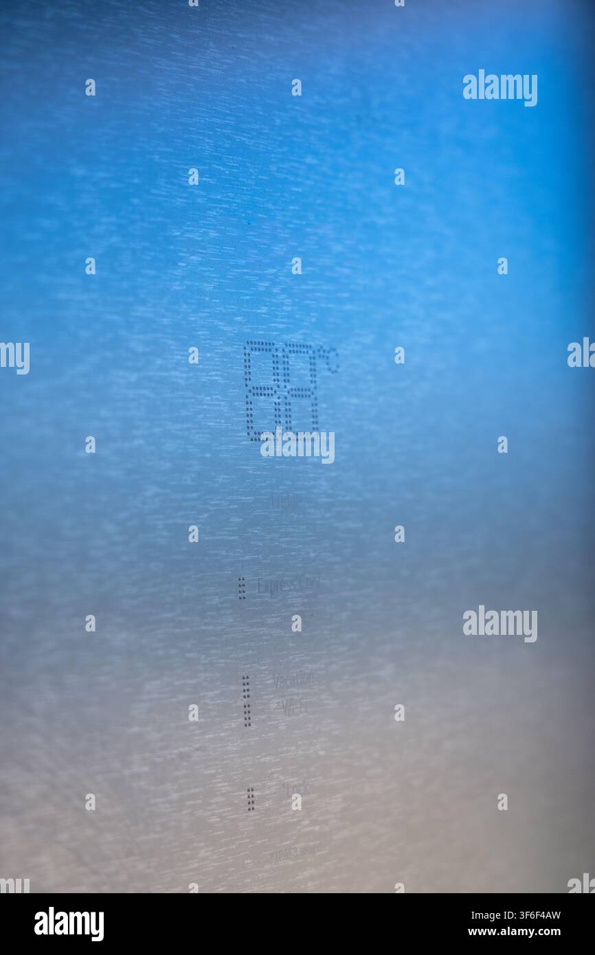 Scatto macro astratto che mostra caratteri e simboli finemente incisi su un piano metallico ruvido, illuminato da un morbido sfumato blu Foto Stock