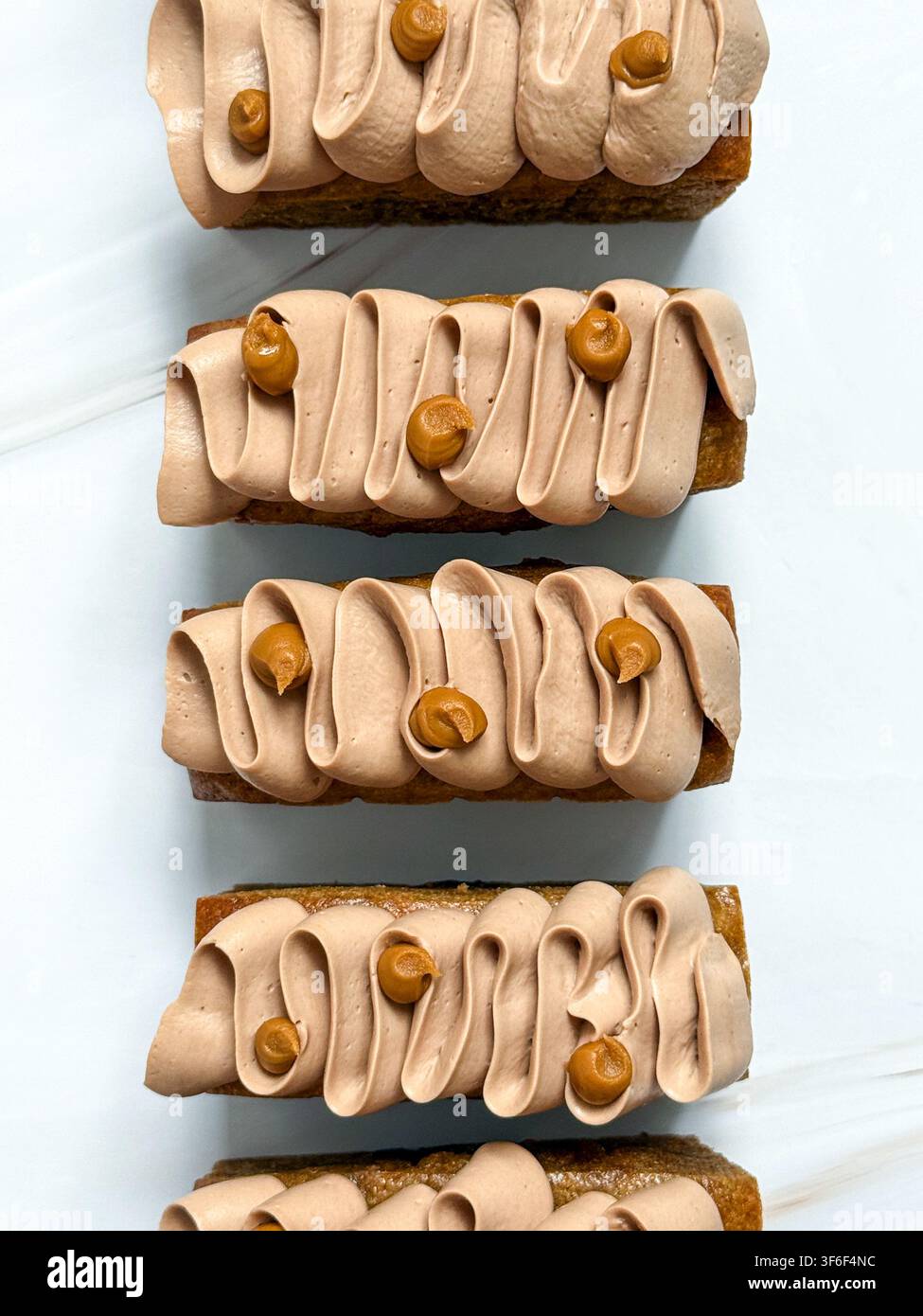 Eleganti mini panini decorati con onde di crema al cioccolato, gocce di caramello e briciole croccanti Foto Stock