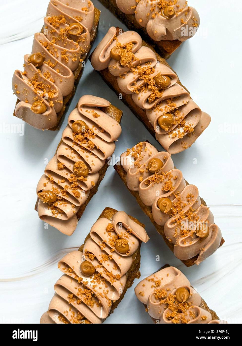 Eleganti mini panini decorati con onde di crema al cioccolato, gocce di caramello e briciole croccanti Foto Stock