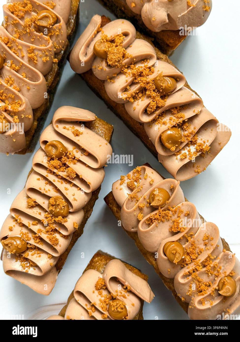 Eleganti mini panini decorati con onde di crema al cioccolato, gocce di caramello e briciole croccanti Foto Stock