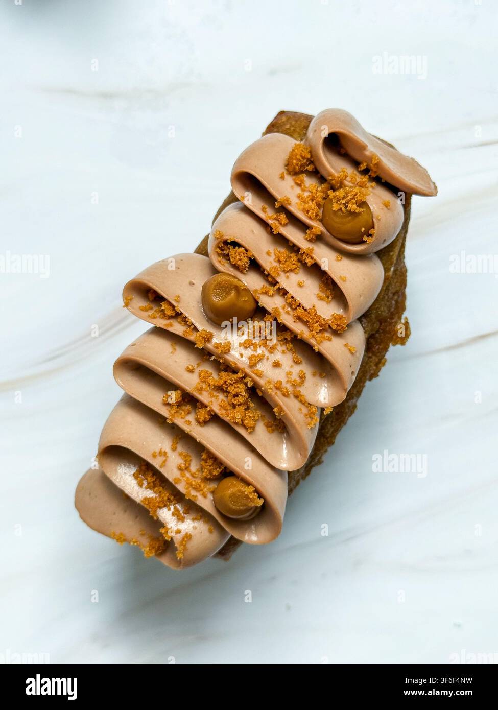Eleganti mini panini decorati con onde di crema al cioccolato, gocce di caramello e briciole croccanti Foto Stock