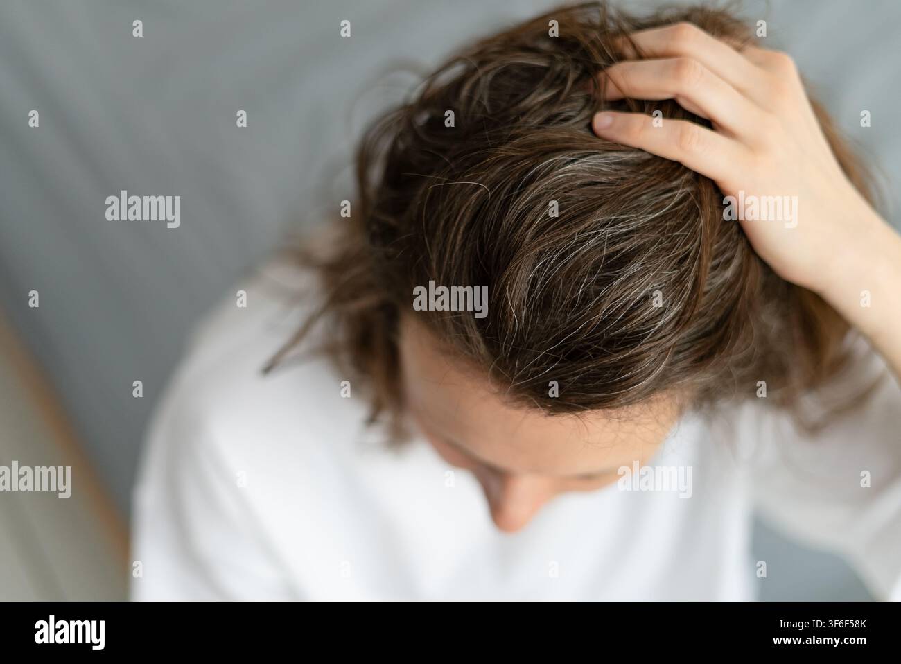 Una donna matura guarda il suo riflesso imparando ad accettare i suoi capelli che ingrigiscono. L'anziana signora abbraccia la transizione naturale con quieta dignità. La madre trova pace con il suo aspetto argentato che cambia. Foto Stock