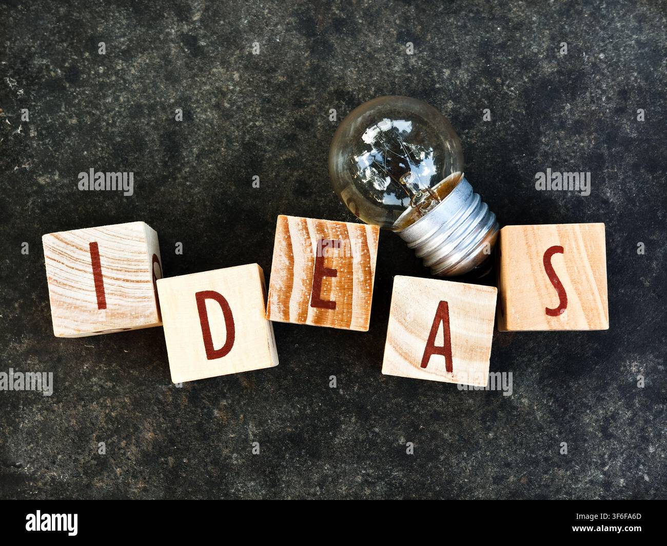 Concetto creativo IDEE con blocchi di lettere in legno leggermente impilati e lampadina su sfondo scuro Foto Stock