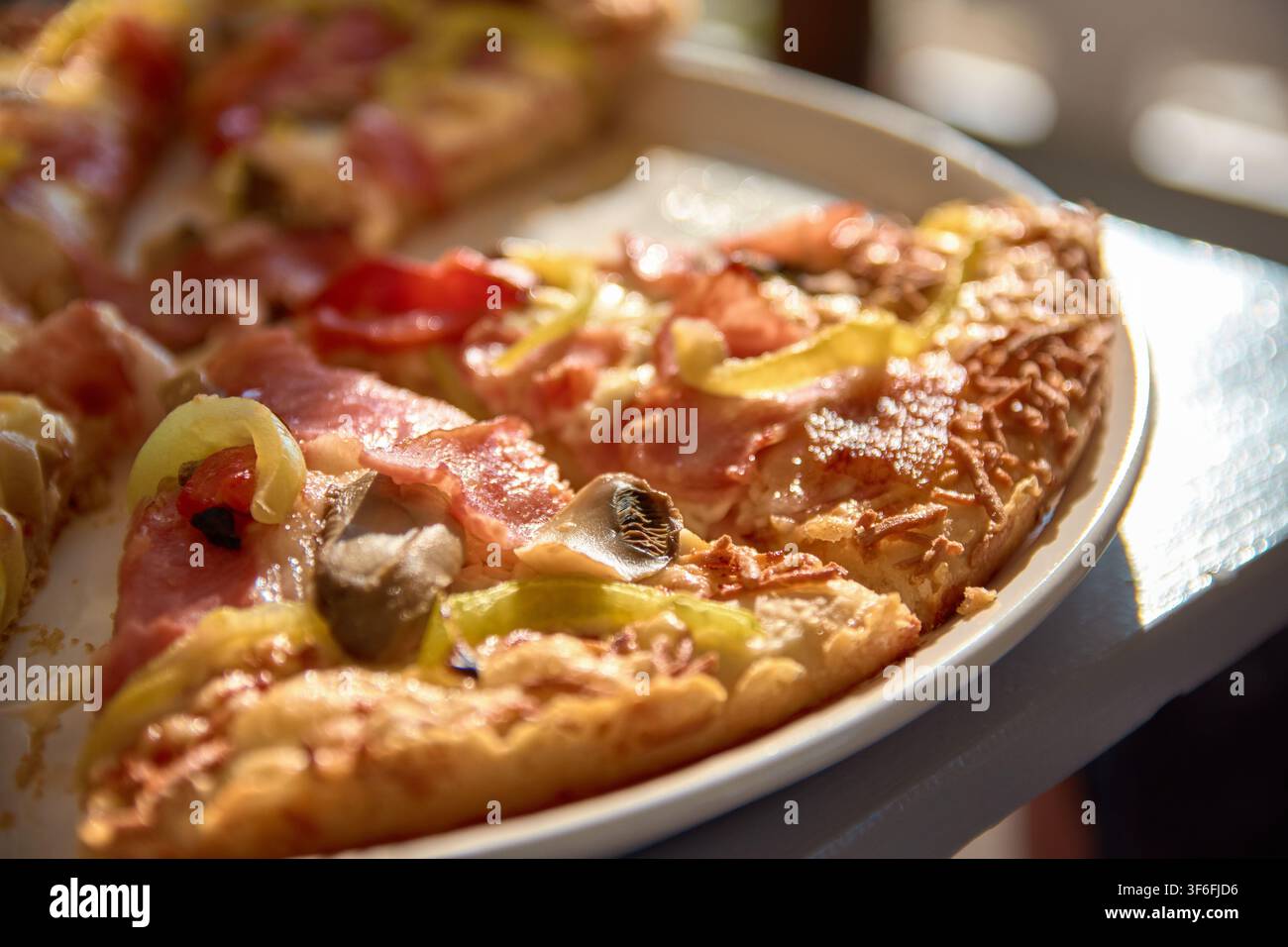 Una vista ravvicinata di fette di pizza appena sfornate ricoperte di formaggio fuso, prosciutto, funghi e peperoni, servite su un piatto bianco. Foto Stock