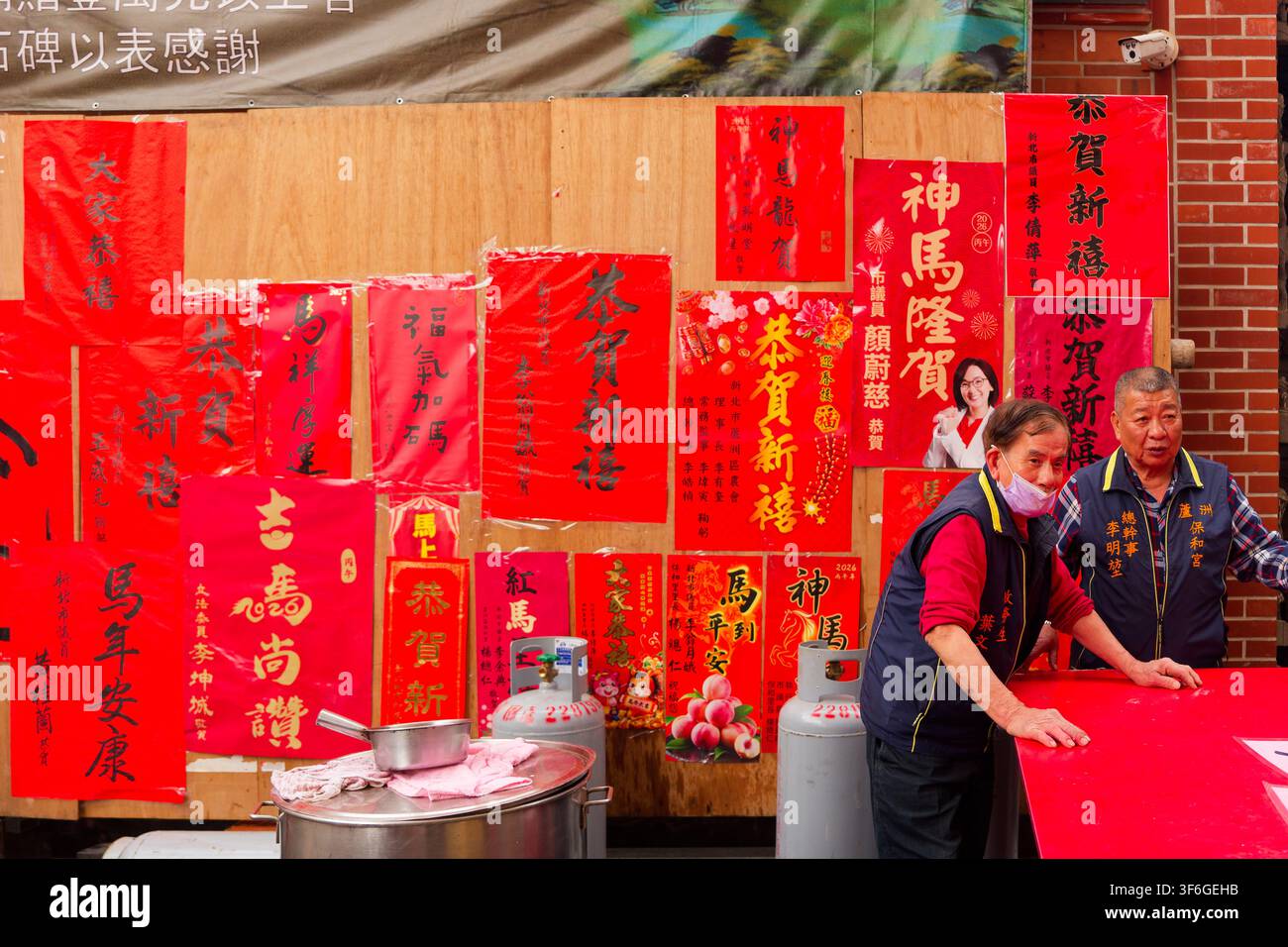Nuova Taipei, Taiwan - 17 feb 2026: segretario del tempio in piedi vicino a coppie di politici rosse al tempio Luzhou Baohe durante il Capodanno lunare Foto Stock