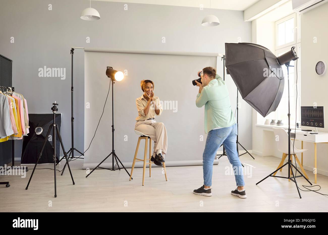 Fotografo cattura un modello allegro su uno sgabello in studio utilizzando l'illuminazione a softbox Foto Stock