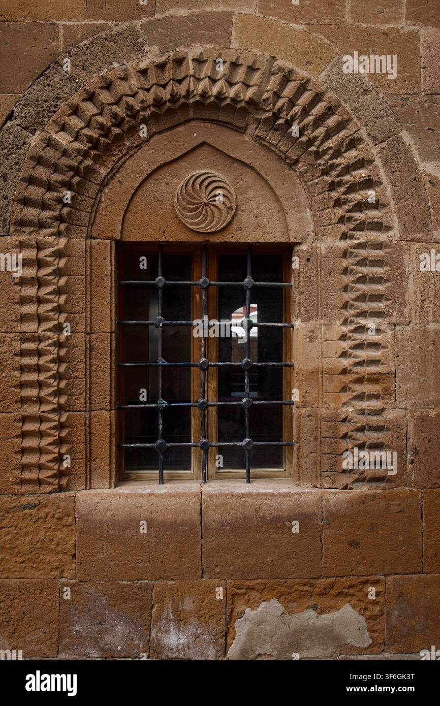 Intrecciata scultura in pietra e motivo della ruota della fortuna su una finestra ad arco selgiuchide storica con sbarre di ferro ad Ahlat, Bitlis, Turchia. Foto Stock