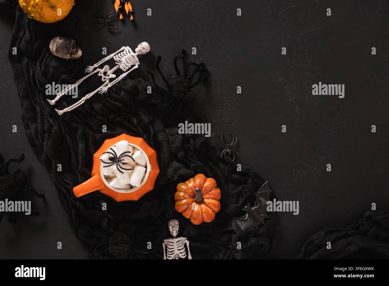 Vista dall'alto di una tazza arancione con cioccolata calda e marshmallow circondata da decorazioni di Halloween su sfondo nero. Bevanda autunnale festosa con spazio libero Foto Stock