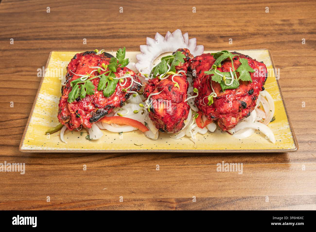 Pezzi di pollo tandoori arrostiti guarniti con coriandolo e germogli su un letto di cipolle Foto Stock