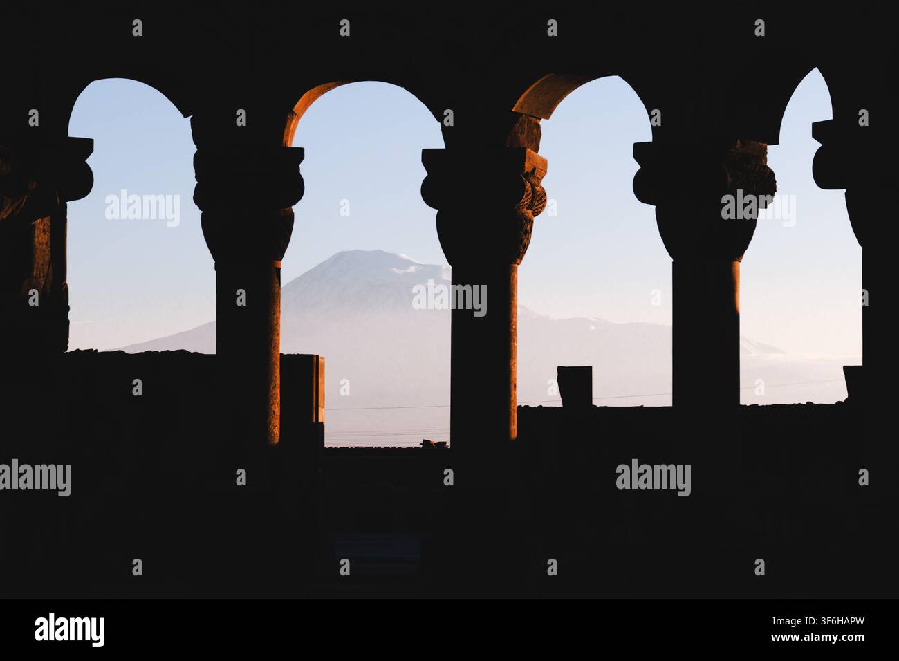 Archi silouettati contro il cielo, in un paesaggio montano, con archi, montagne, da una prospettiva interna che guarda verso l'esterno, con accenti scuri e blu Foto Stock