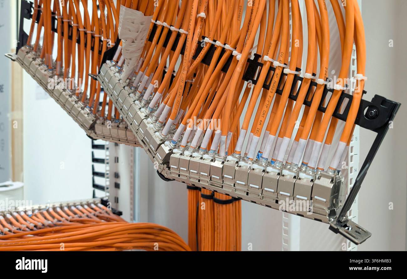 Prima di un pannello di connessione Ethernet ad alta densità con cavi di rete arancioni organizzati installati all'interno di un armadio di comunicazione. Foto Stock