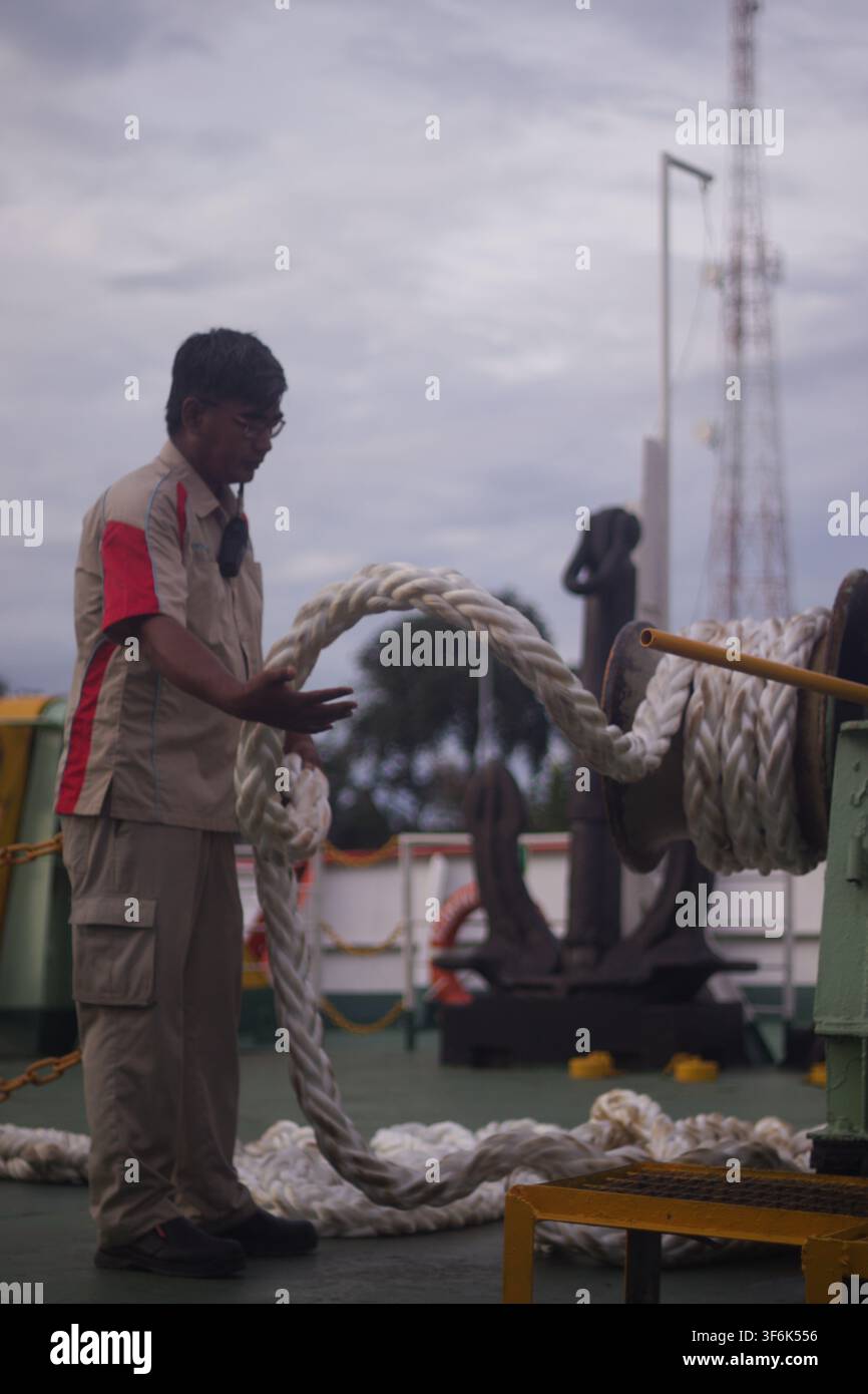 Un operatore di traghetto che maneggia una pesante corda di ormeggio a bordo di una nave al porto di Merak, Banten, Indonesia, il 16 dicembre 2024. Foto Stock