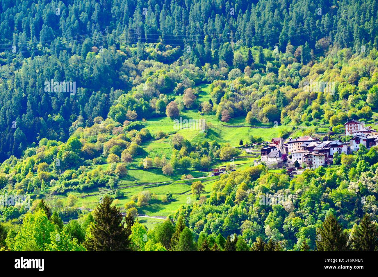 Fotografia paesaggistica in stile aereo orizzontale di un piccolo villaggio remoto arroccato su un vivace pendio montuoso coperto di alberi, circondato da fitte foreste. Foto Stock