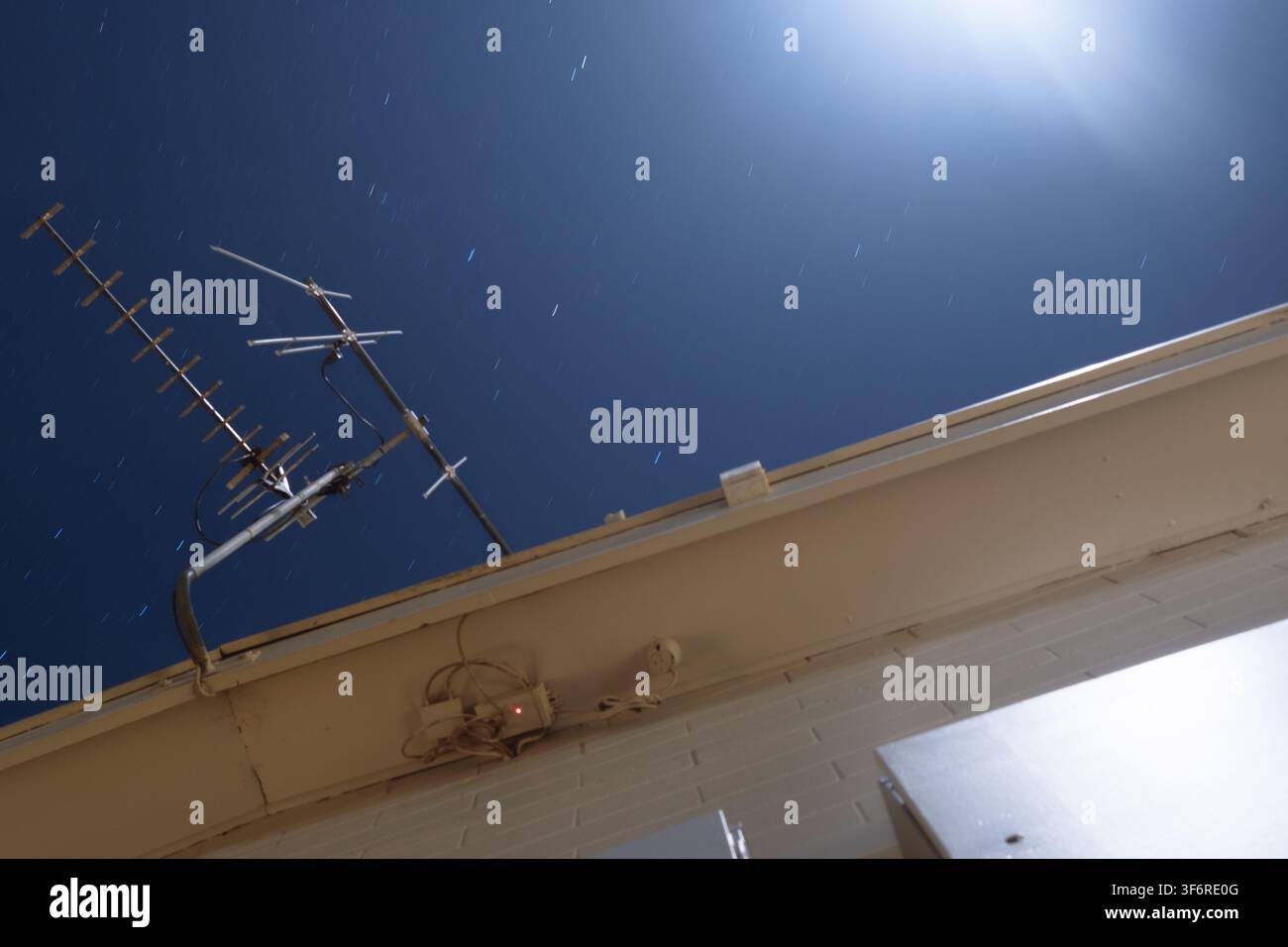 Un cielo stellato brilla sopra un'antenna sul tetto. Scie di stelle con il bagliore della luna. Foto Stock