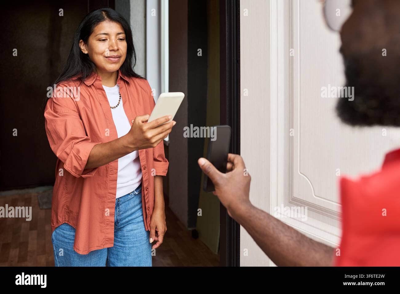 Donna ispanica che scansiona un codice QR sullo smartphone di un fattorino alla porta Foto Stock