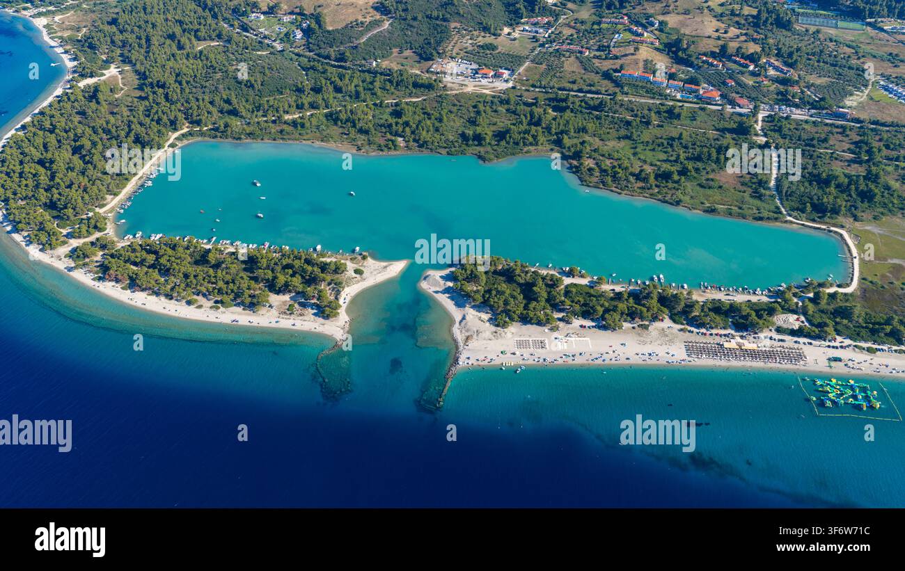 Acqua turchese chiara riempie una laguna costiera accanto a spiagge sabbiose, costa boscosa, barche ancorate e case sparse sulla costa greca. Foto Stock