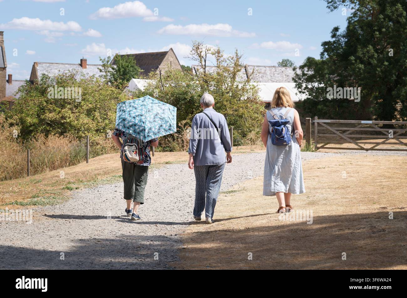 Tre visitatori, uno con un ombrello, in viaggio verso il Chester House Estate, Wellingborough, Inghilterra, in una calda giornata estiva. Foto Stock