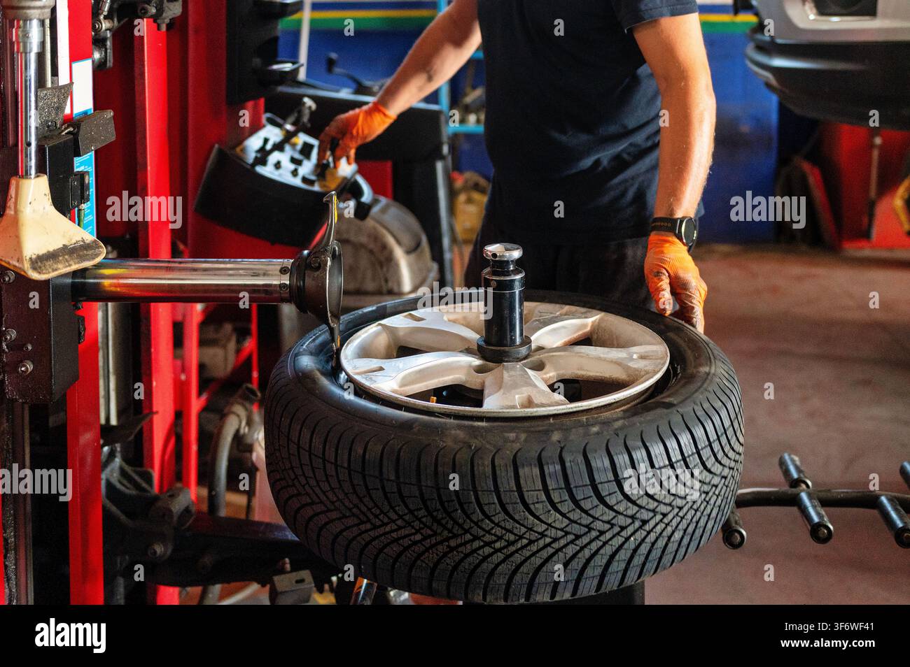 Meccanico automobilistico che cambia una gomma utilizzando una macchina professionale per il cambio gomme in officina, mostrando operazioni di montaggio della ruota e servizio gomme. Foto Stock