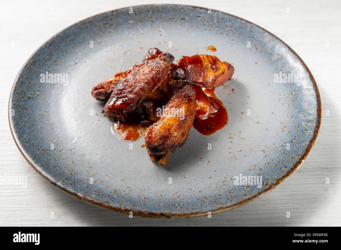 Alette di pollo al BBQ glassate con una ricca salsa barbecue, arrostite fino a renderle croccanti e caramellizzate, servite come antipasto saporito su un piatto di ceramica blu Foto Stock