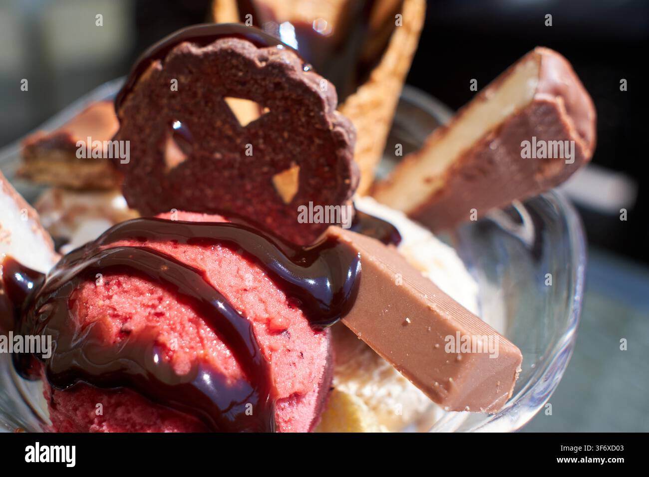 Un primo piano di un delizioso dessert con gelato alla fragola ricoperto di sciroppo di cioccolato, guarnito con biscotti croccanti, barrette di waffle e una cialda Foto Stock