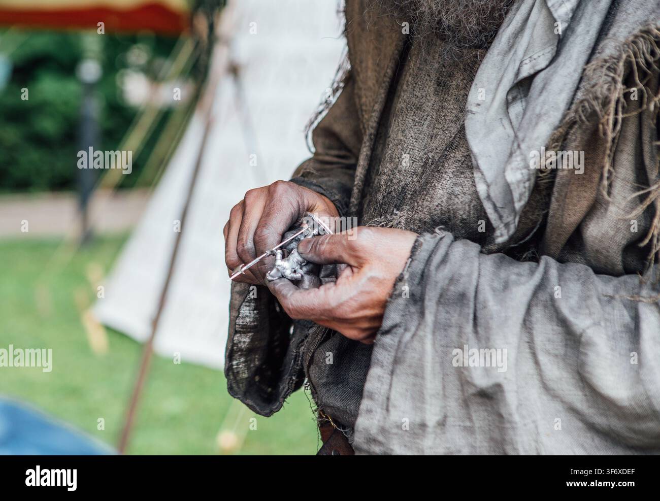 Artigiano del festival medievale che crea miniature in metallo fatte a mano con attrezzi, rievocazione storica, processo di officina artigiana all'aperto Foto Stock