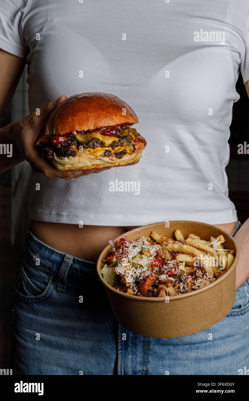 Donna che tiene un doppio cheeseburger e una ciotola di cibo Foto Stock