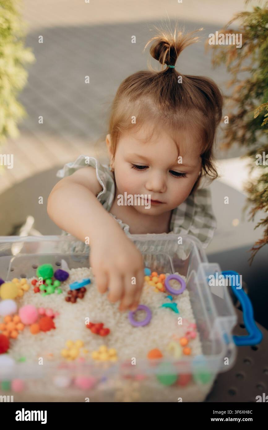 Bambino che esplora un contenitore di riso sensoriale durante lo sviluppo della motricità fine Foto Stock