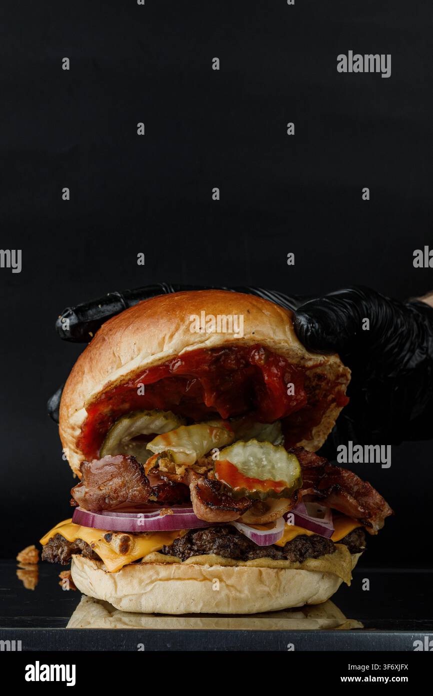 Mano guantata assembla un gigantesco cheeseburger al bacon Foto Stock