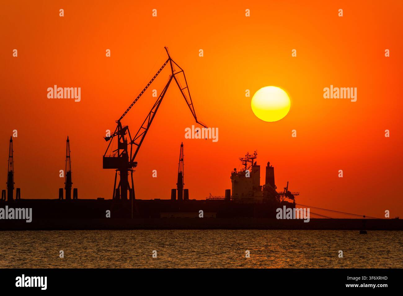 Infrastruttura industriale e marittima silouettata contro un tramonto drammatico sul Mar Bohai, vista da Shanhaiguan, Qinhuangdao, Cina Foto Stock