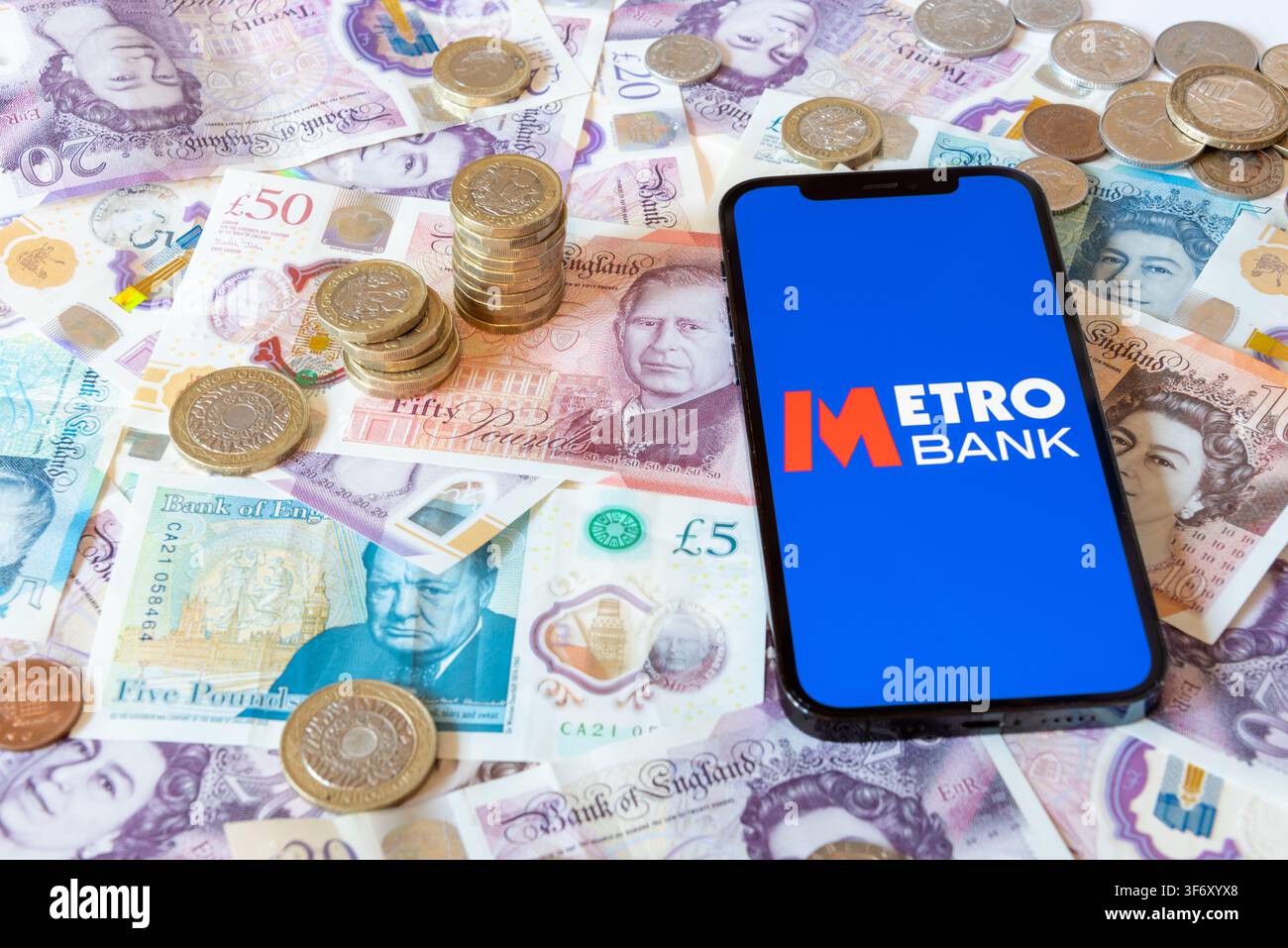 App Metro Bank con banconote e monete in sterline in sfondo Foto Stock