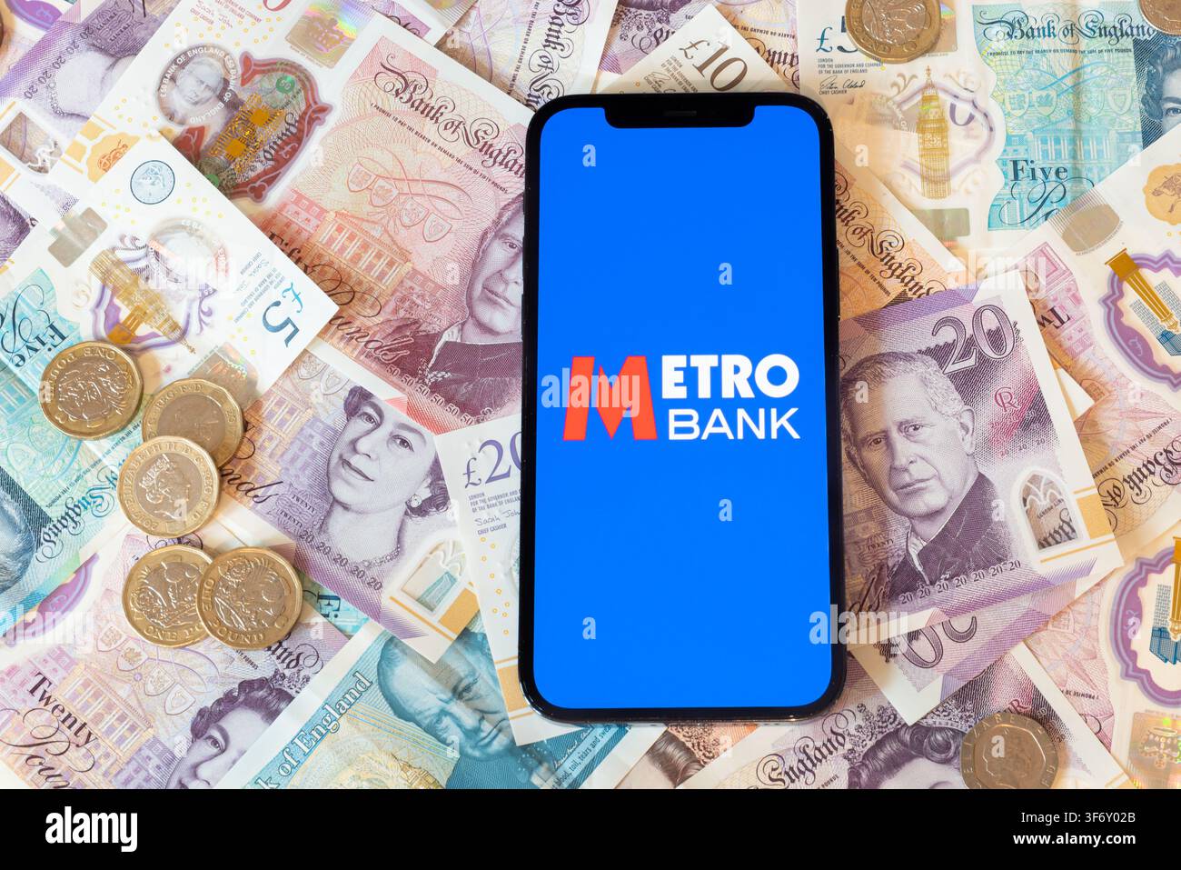 App Metro Bank con banconote e monete in sterline in sfondo Foto Stock