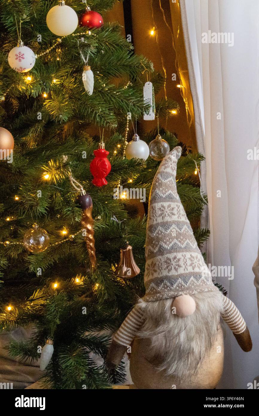 Albero di Natale decorato con ornamenti, palline e luci calde a stringa brilla in un ambiente festivo domestico. Concetto di decorazione tradizionale per le feste e wa Foto Stock