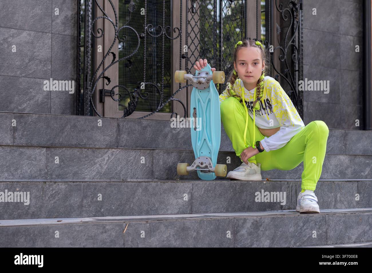 Ragazza skater seduta sui gradini di granito di un edificio. Concetto: Ritorno a scuola stile di strada giovanile, Stile di vita autunnale attivo, Tendenze adolescenziali. Foto Stock