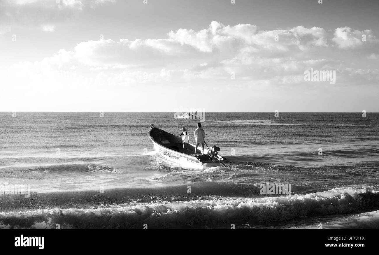 Paesaggio monocromatico che cattura pescatori che si spingono verso il mare in un piccolo motoscafo vicino alla riva. Foto Stock