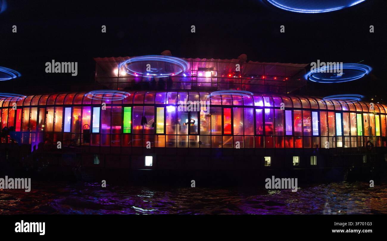 Barca da festa illuminata che naviga di notte con luci multicolori vibranti che si riflettono sull'acqua. Foto Stock