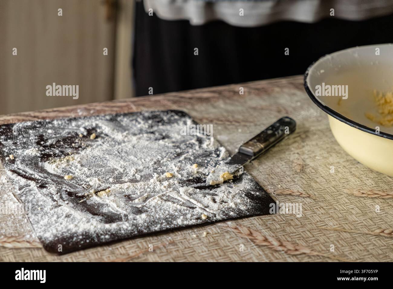 Tagliere infarinata con un coltello e una ciotola per mescolare su un tavolo da cucina durante la preparazione di pancake tradizionali al formaggio fresco per evidenziare l'autenticità Foto Stock