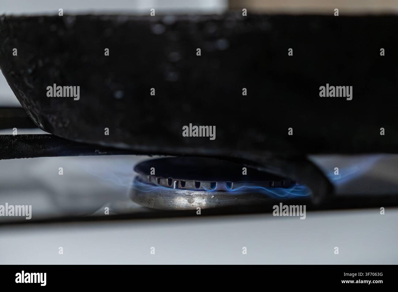 Padella nera posizionata su una fiamma blu brillante di un fornello a gas, evidenziando il calore e l'energia culinari utilizzati per cuocere torte di pasta mentre evoca un Foto Stock