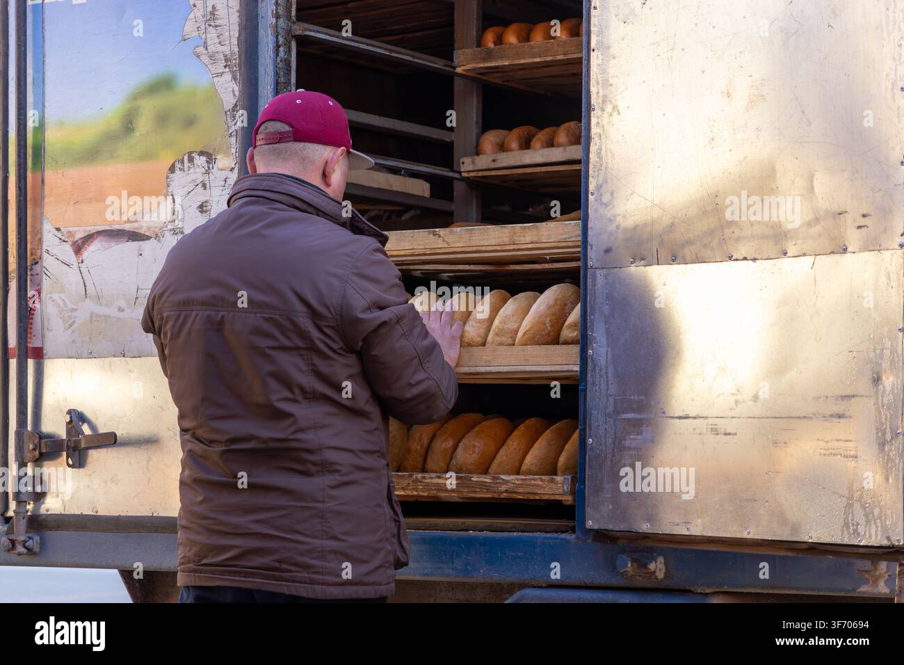 Corriere professionista che carica pane rustico in un veicolo di stoccaggio per la distribuzione mattutina, sottolineando la produzione locale di alimenti, un servizio di consegna affidabile Foto Stock