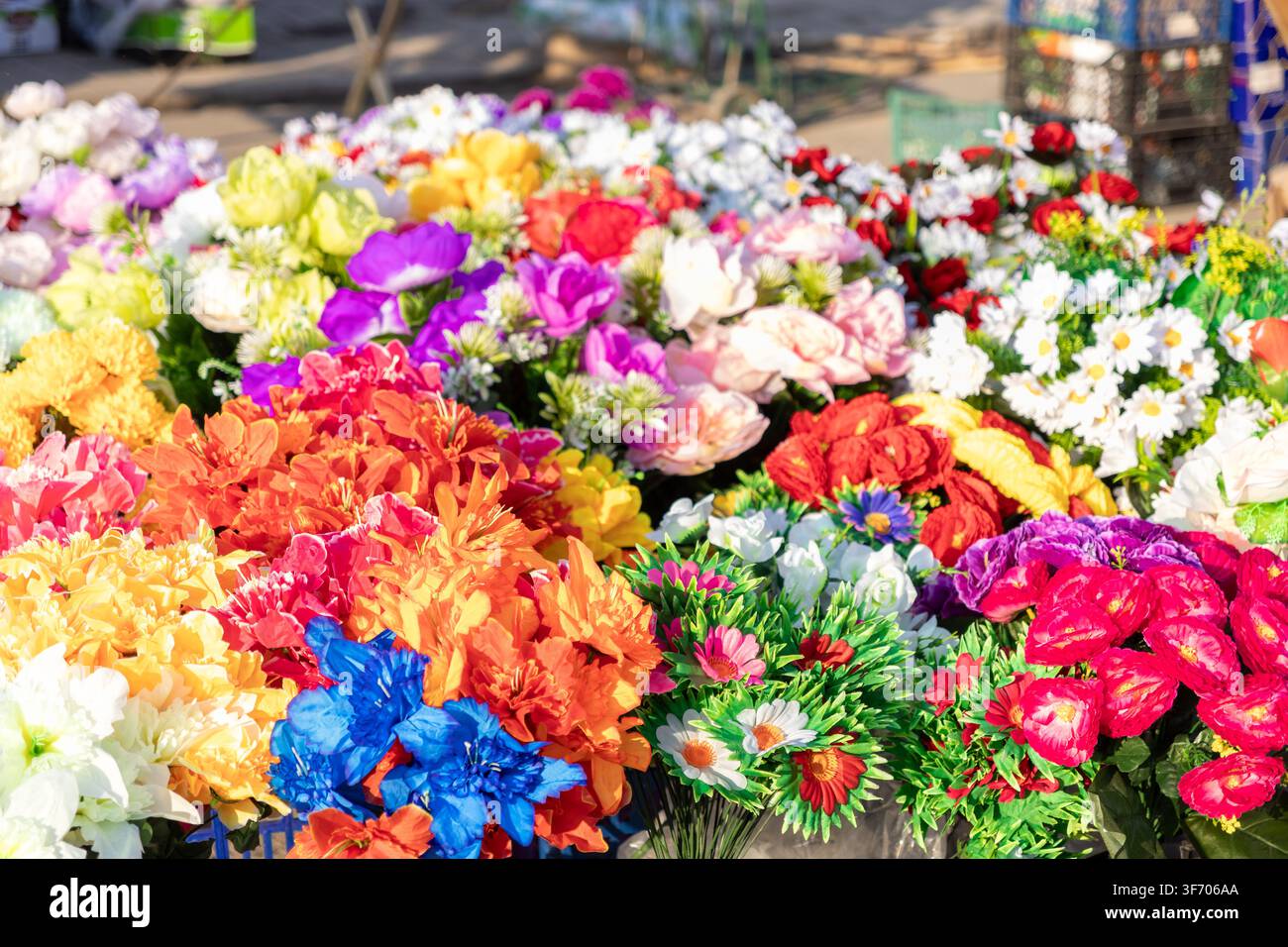 Collezione varia di fiori di seta colorati disposti in un mercato di strada soleggiato, rappresentanti un'estetica festiva e decorativa per progetti di design floreale Foto Stock
