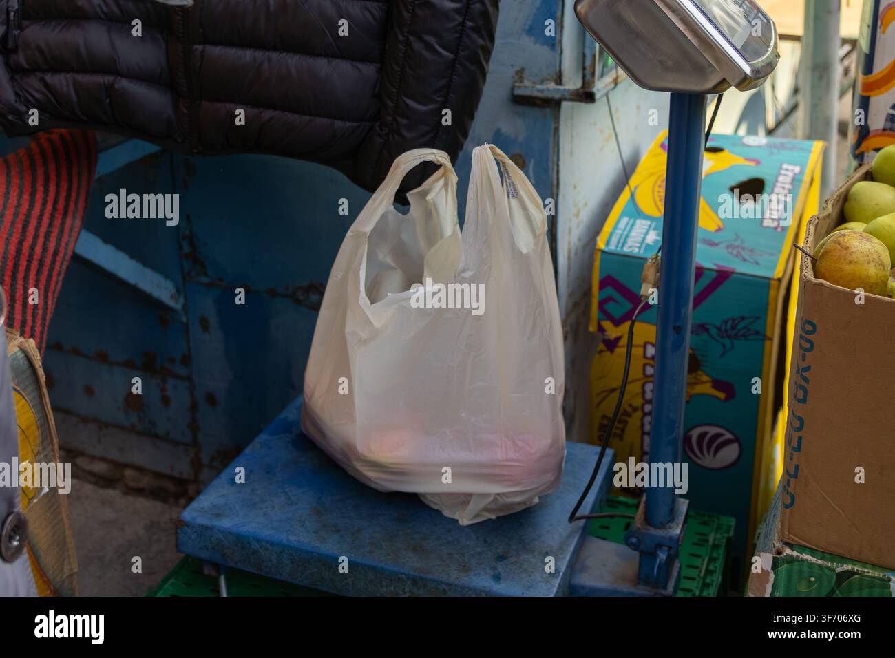 Horodok, Ucraina - 25 marzo 2026: Una borsa della spesa in plastica traslucida vuota poggia su una bilancia commerciale a una bancarella di frutta per evidenziare la quotidianità Foto Stock