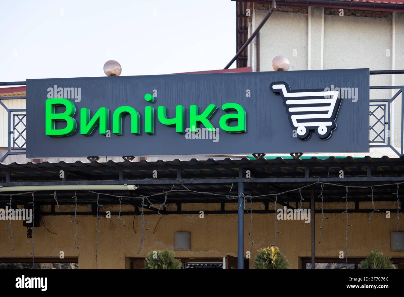 Horodok, Ucraina – 25 marzo 2026: Insegna della vetrina della panetteria con testo verde e un simbolo di carrello sopra l'ingresso di un edificio commerciale, che illustra s Foto Stock