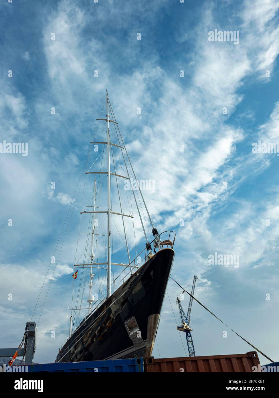 Un grande barca a vela è ormeggiata in un porto industriale. Gru industriali sono visibili sullo sfondo sotto un cielo nuvoloso. La scena mostra activi Foto Stock