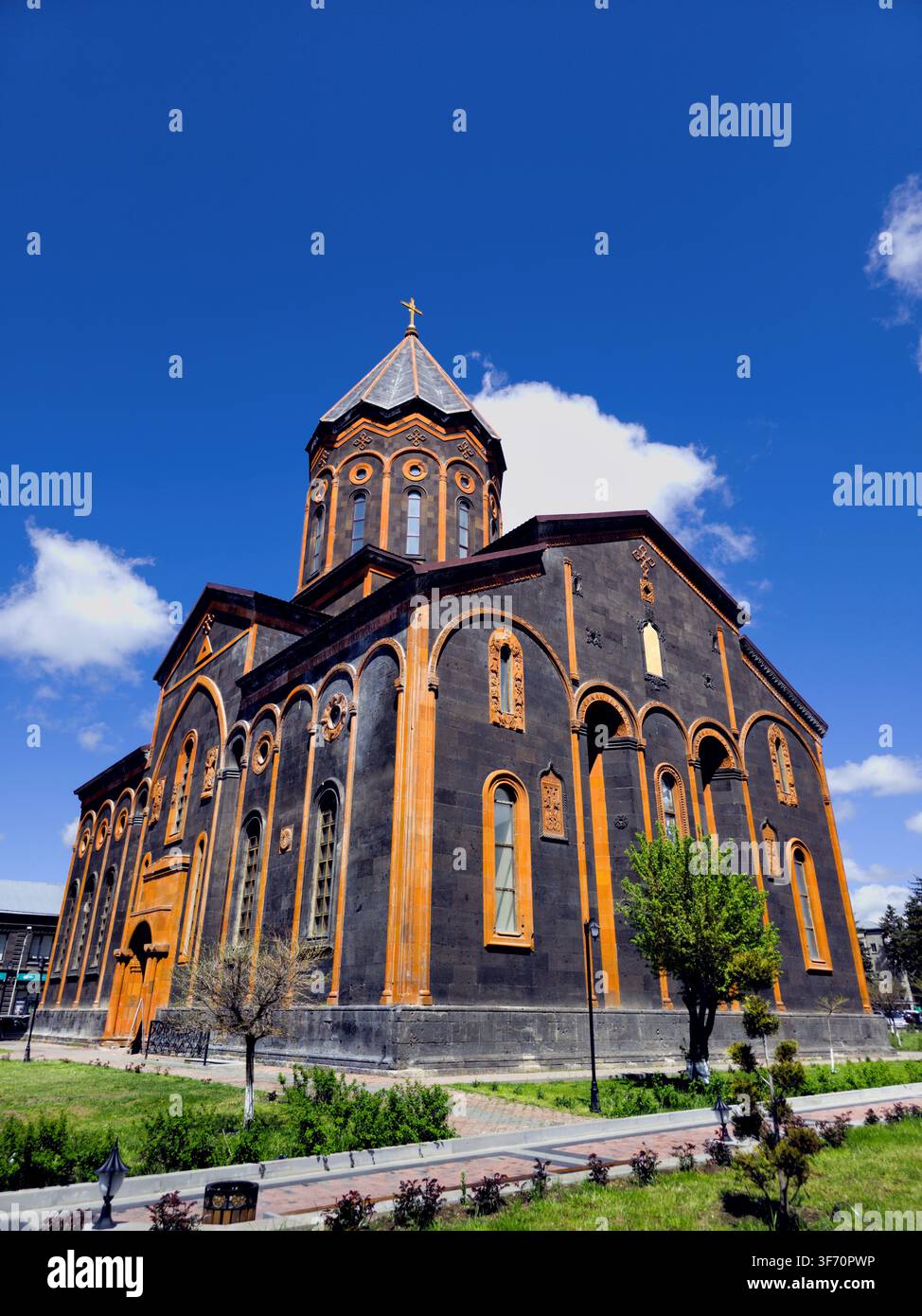 Chiesa del Santo Salvatore con mura di pietra scura e dettagli in legno sotto un cielo blu brillante. Prati verdi e alberi circondano l'edificio Foto Stock