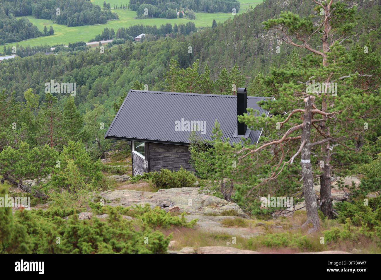 Piccolo capanno moderno in legno su una montagna, circondato da un paesaggio naturale sotto un cielo estivo sereno. Foto Stock